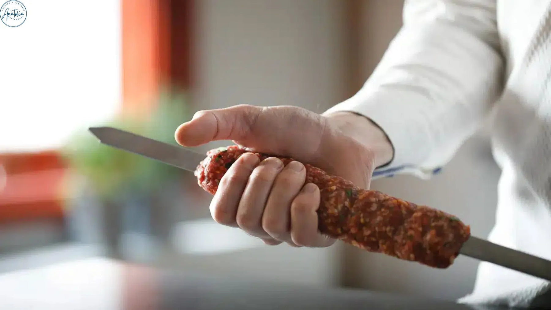 Chef hand-pressing minced lamb Adana kebab onto a flat skewer