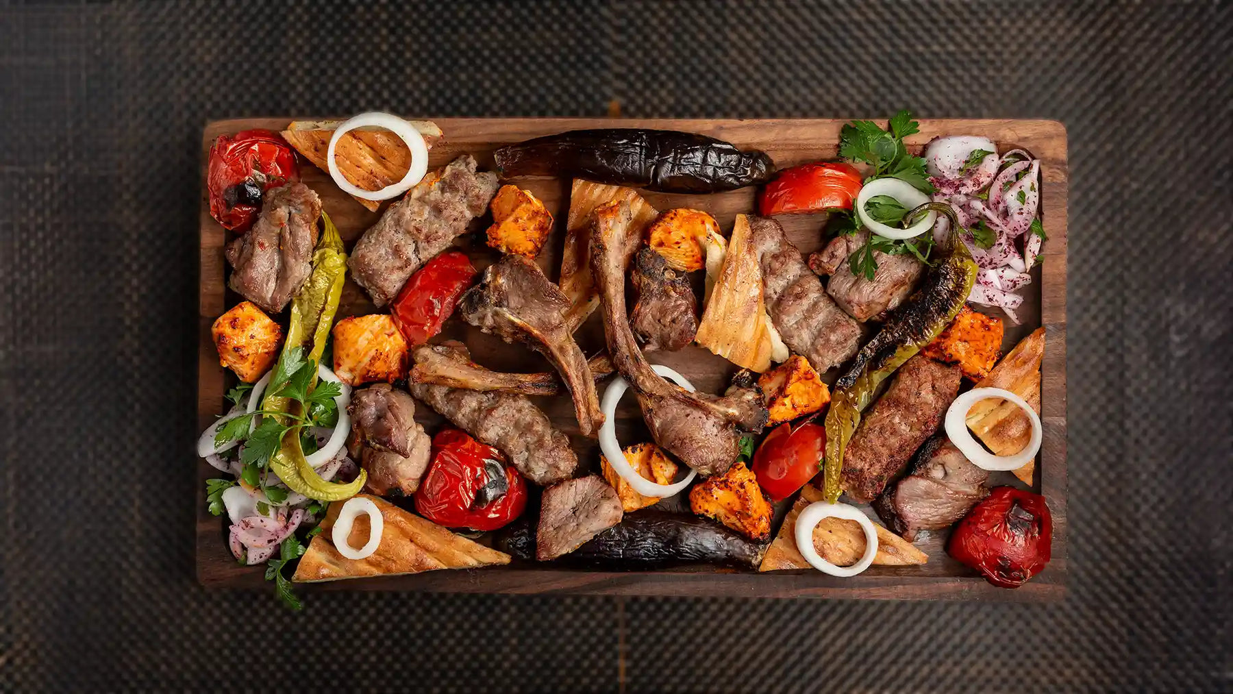 Top-down view of a rich mixed kebab platter at Anatolia Restaurant, showcasing some of the best halal food in Singapore with grilled meats, chops, and vegetables on a wooden board.