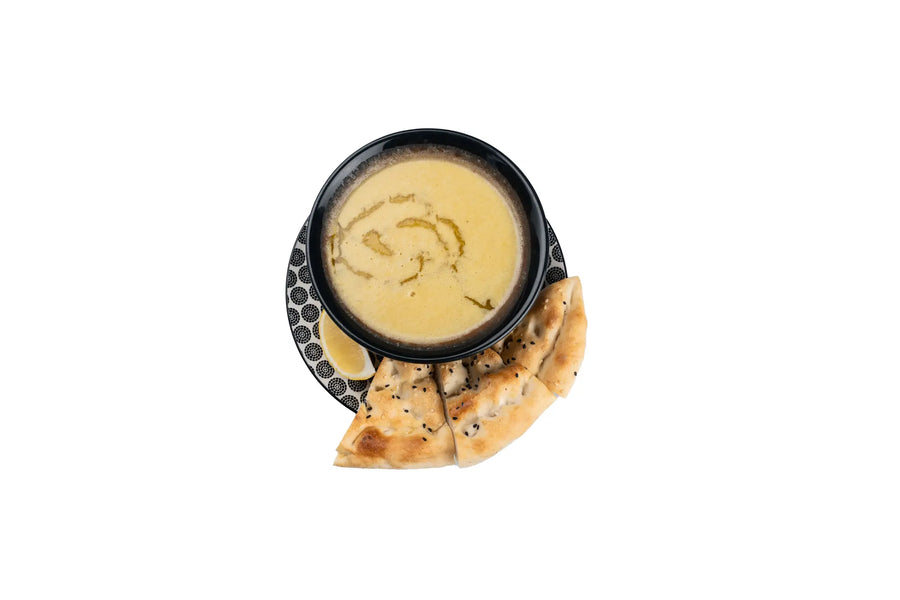 Creamy soup served in a black bowl with sliced Turkish bread and a lemon wedge on the side.